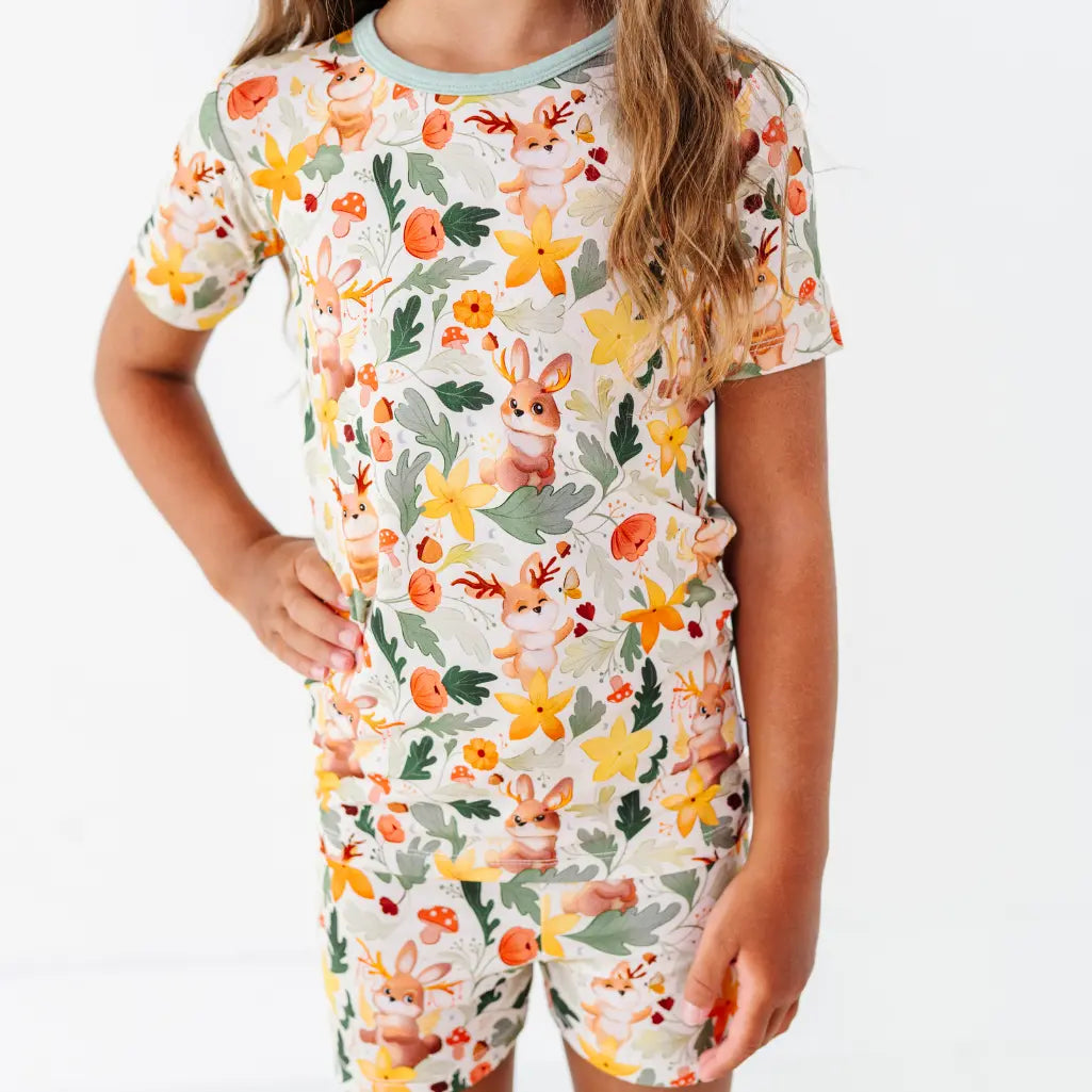 A close up of a child wearing a short sleeve pajama top and shorts with sage trim in a woodland jackalope print.